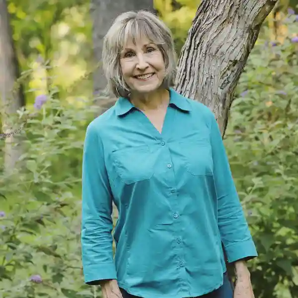 A woman standing in front of trees and bushes.