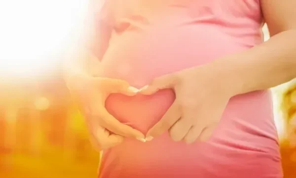 A pregnant woman holding her stomach with hands.