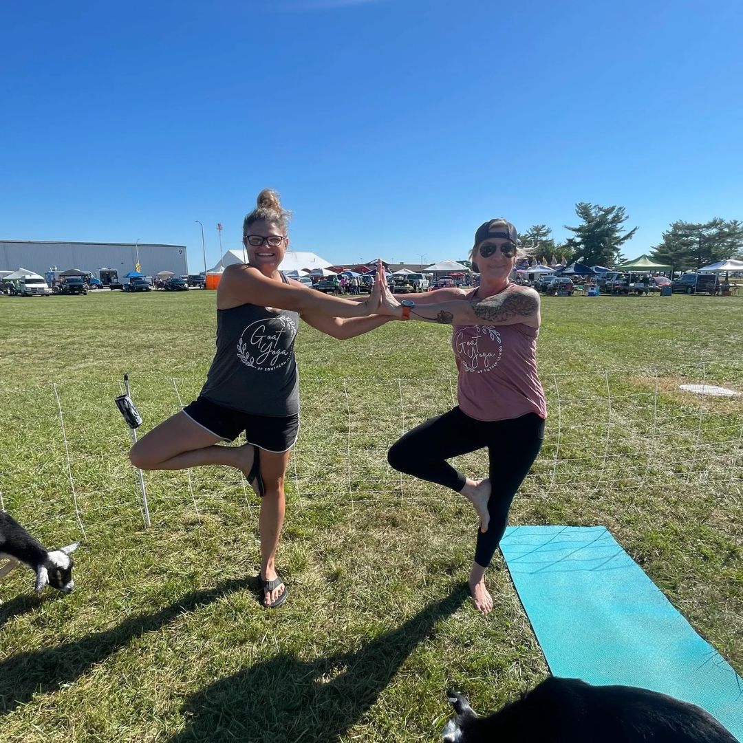 Two women doing yoga in a field with their dogs.