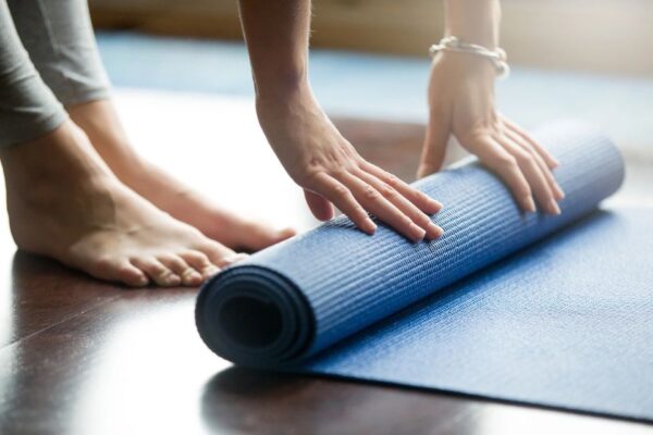 A person rolling up a blue yoga mat.